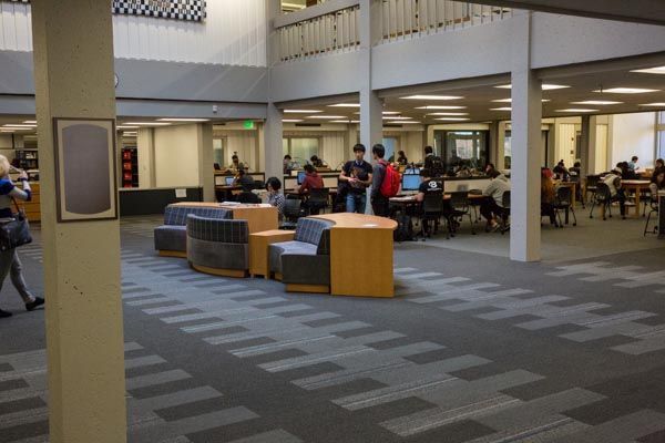 Indoor library lounge with tables, chairs, and people seated in a spacious open area