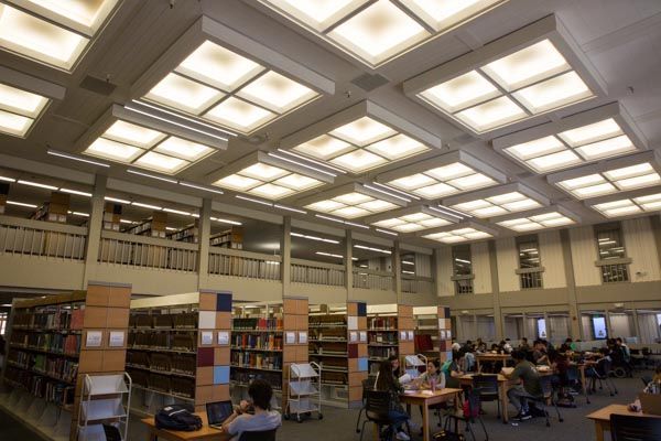 Public library reading room with bookshelves, tables, and people studying under bright ceiling lights