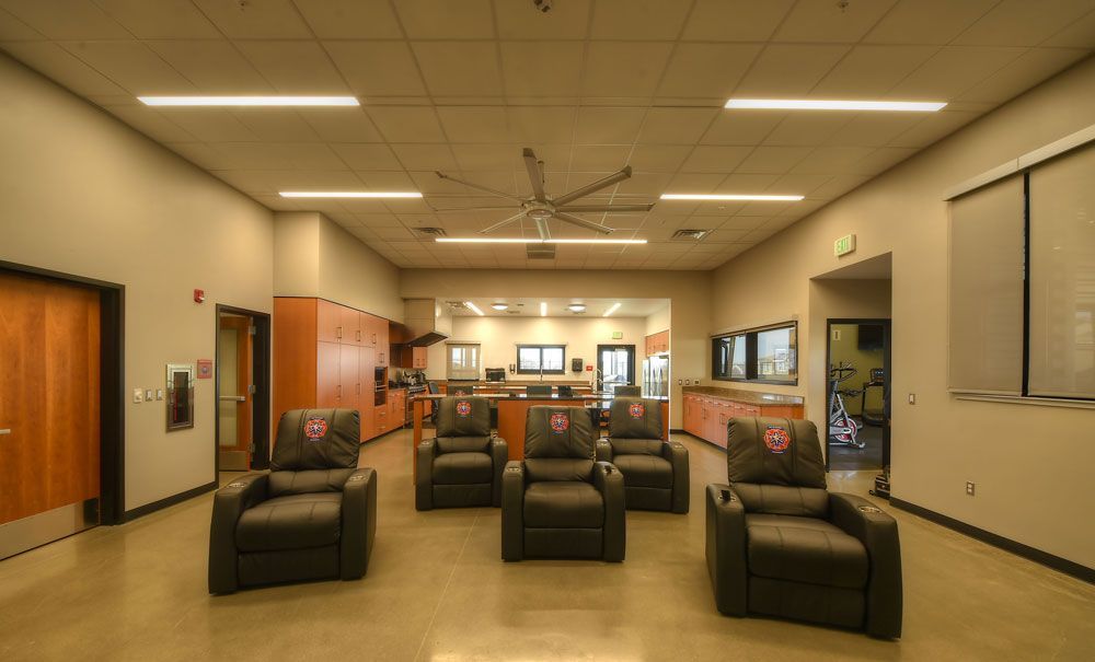 Empty waiting room with black chairs, beige walls, overhead lights, and a service counter in back