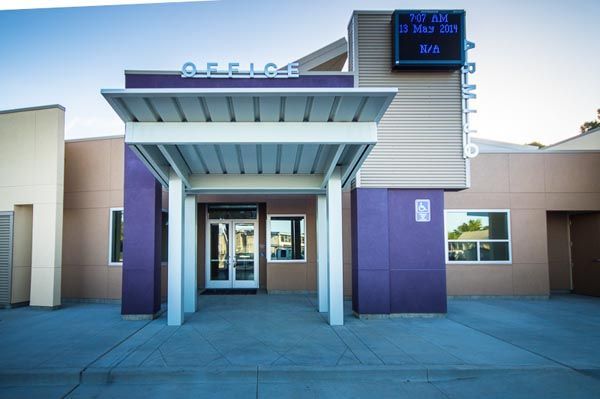 Front entrance of a modern building with a covered walkway and purple columns