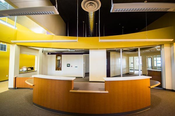 Modern empty lobby with yellow walls, curved wooden reception desk, and overhead lighting