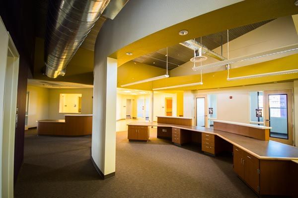 Empty office interior with curved desks, yellow walls, and exposed ceiling ducts