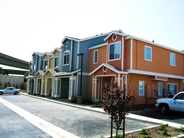 Row of colorful townhomes with parked cars and a covered driveway on a sunny day