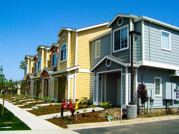 Row of colorful modern townhouses with small front lawns on a sunny street