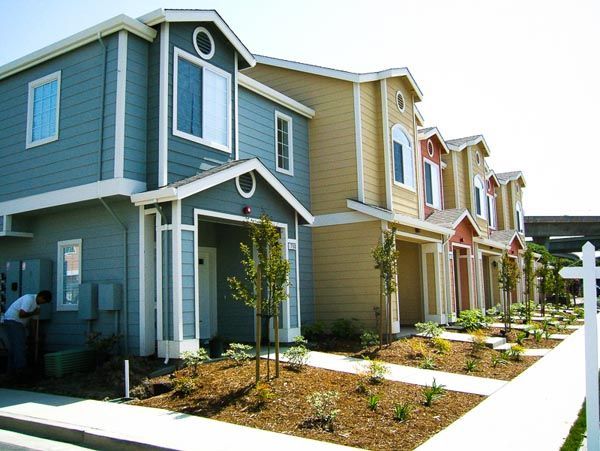 Row of colorful townhouse homes with small landscaped front yards and a sidewalk
