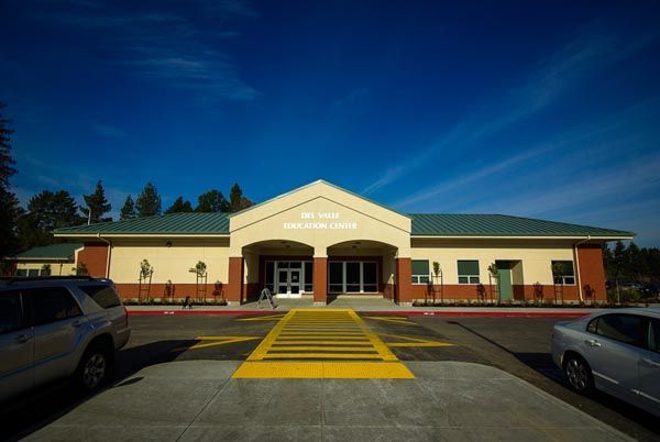 Front entrance of a beige building with a green roof and yellow striped walkway at dusk