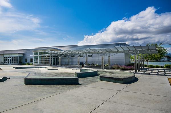 Modern building entrance with glass canopy, benches, and open paved courtyard under a cloudy sky