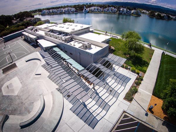 Aerial view of a modern lakeside building with solar panels and a waterfront walkway