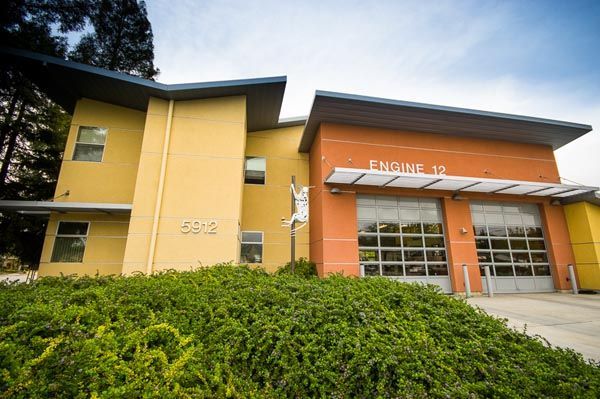 Modern yellow and orange building entrance with glass garage doors and bushes in front