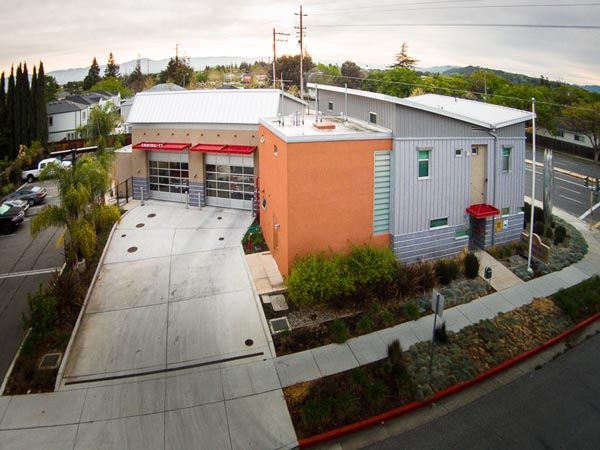 Aerial view of a modern building with a curved driveway, red awning, and surrounding trees and parking area