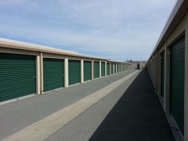 Storage unit corridor with green roll-up doors and a long, empty walkway