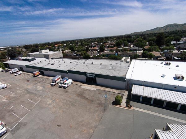 Aerial view of a large warehouse with parked trucks and a suburban neighborhood beyond