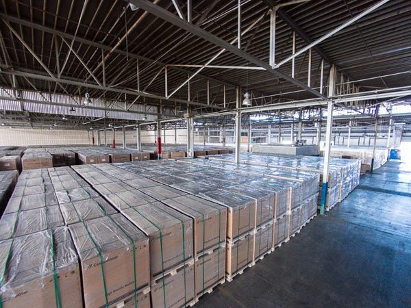 Warehouse with rows of palletized boxes under a high metal roof, lit by skylights