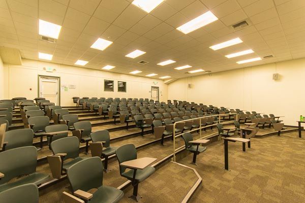 Empty lecture hall with rows of gray seats and desks under bright ceiling lights