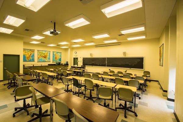 Empty classroom with rows of desks, chalkboard, world maps, and fluorescent ceiling lights
