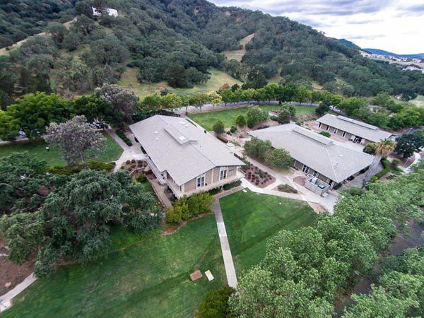 Aerial view of two modern buildings with green lawns and forested hills behind them.