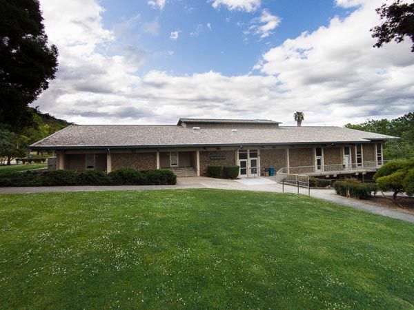 Single-story brick building with a wide lawn, cloudy sky, and covered entrance.