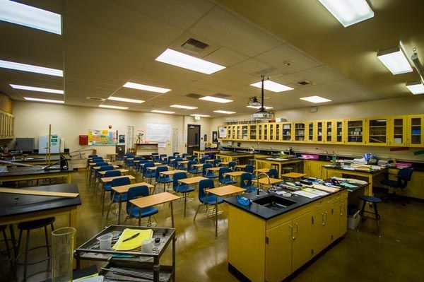 Empty school science lab with blue stools, lab tables, and cabinets under fluorescent lights