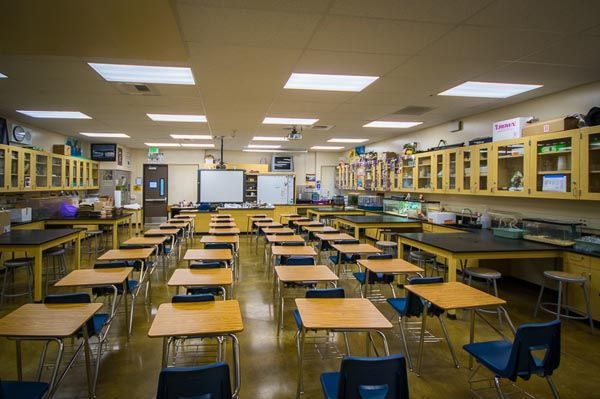 Empty classroom with rows of desks, chairs, and a whiteboard at the front under fluorescent lights