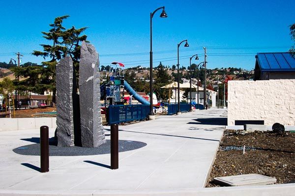 Outdoor playground with climbing structure, slides, and blue-roofed shelter on a sunny day
