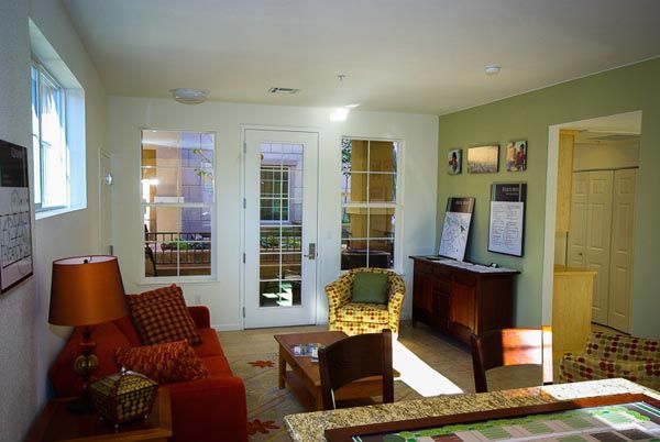 Bright living room with red armchair, wicker chair, desk, and sunlit French doors.