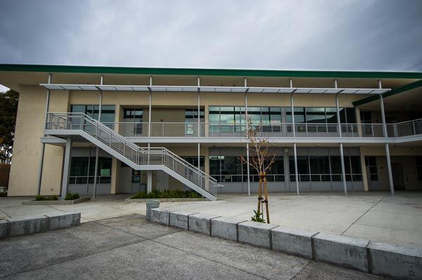 Modern two-story building with an exterior staircase and wide glass facade in a paved courtyard