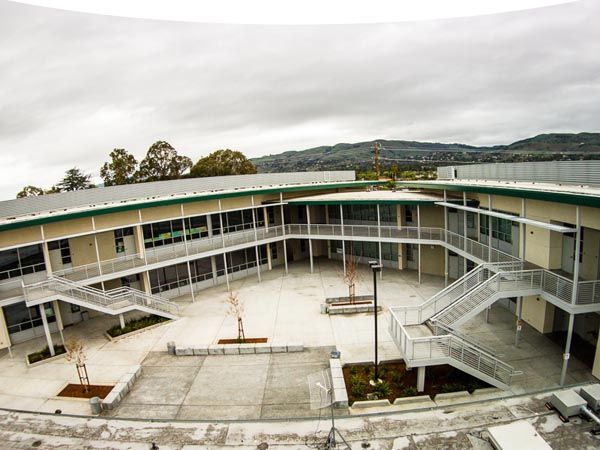Courtyard view of a two-story school building with covered walkways and stairs under an overcast sky