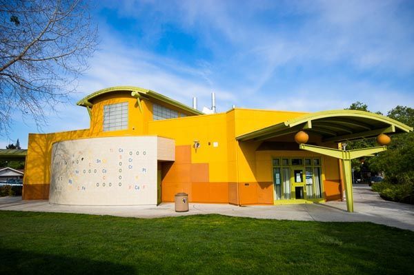 Bright yellow modern building with curved roof, green lawn, and blue sky