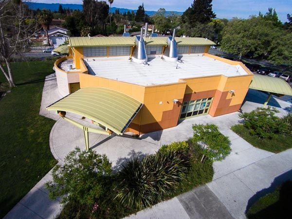 Orange building with white roof and green awnings, seen from above amid trees and pathways