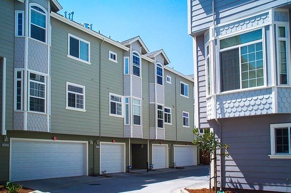 Apartment complex with attached garages, gray and green siding, under a clear blue sky