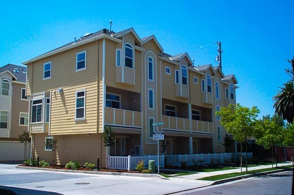 Three-story beige apartment building on a sunny street corner with balconies and white trim
