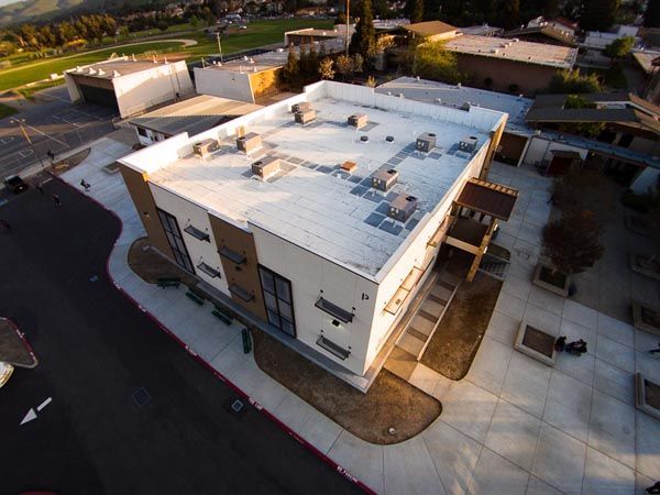 Aerial view of a modern white commercial building with parking lots and surrounding roads.