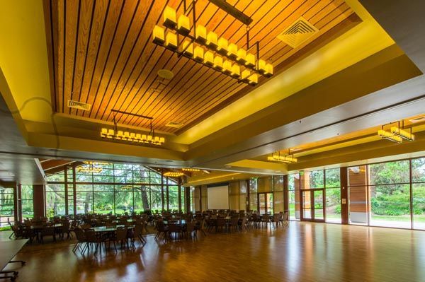 Empty modern dining hall with bright yellow ceiling, large windows, and views of greenery outside
