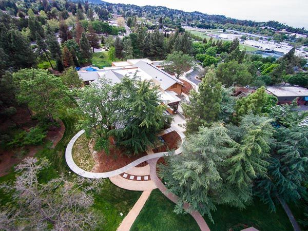 Aerial view of a large house surrounded by lush trees and landscaped paths