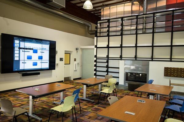 Modern classroom with desks, wall-mounted screen, and large windows with black grid frames