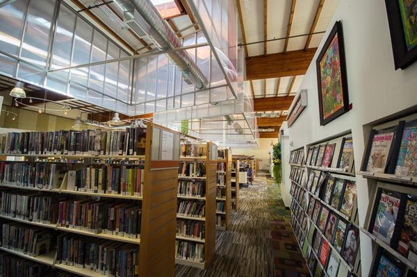 Library aisle with bookshelves and tall windows under a bright glass ceiling