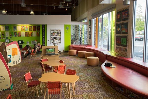 Bright children's playroom with colorful furniture, low tables, rugs, and large windows along the right wall