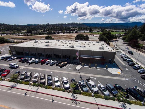 Aerial view of a low beige commercial building with a full parking lot and mountains in the background