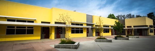 Yellow school building with a courtyard and small trees under a clear sky