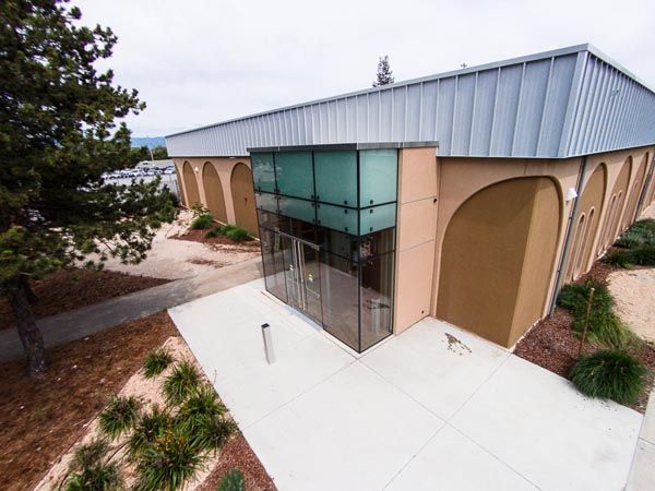 Modern building entrance with tan arches, glass doors, and a white concrete patio