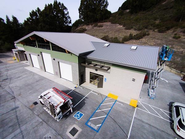 Aerial view of a small industrial building with loading bays, parking spaces, and a trailer in front.