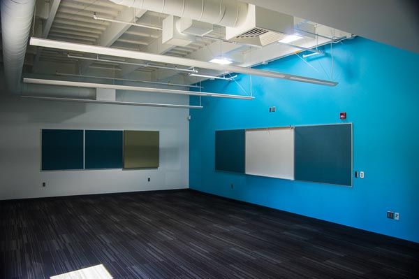 Empty modern room with blue accent wall, dark floor, and mounted whiteboards and acoustic panels