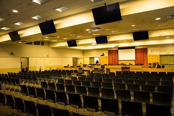 Empty auditorium with rows of black chairs and a stage under warm ceiling lights
