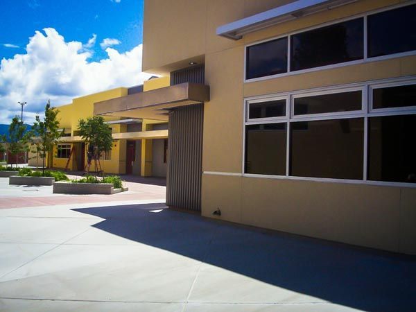 Modern building entrance with beige walls, large windows, and a sunny courtyard under a blue sky