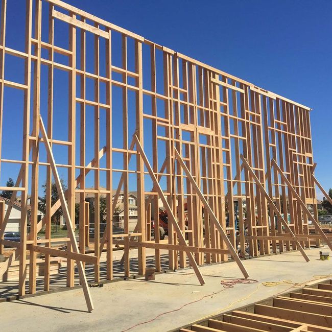 Wooden house framing under construction against a clear blue sky, with exposed studs and roof trusses