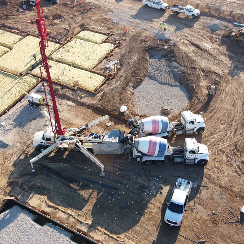 Aerial view of concrete trucks and a pump at a busy construction site with foundation slabs.