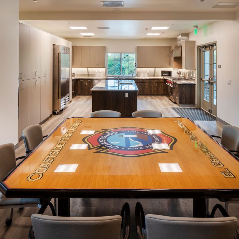 Conference room with a large wooden table, kitchen area, and glass doors in the back.