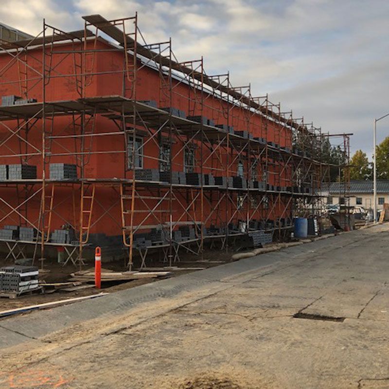 Scaffolding surrounds a red building under construction on a concrete lot.