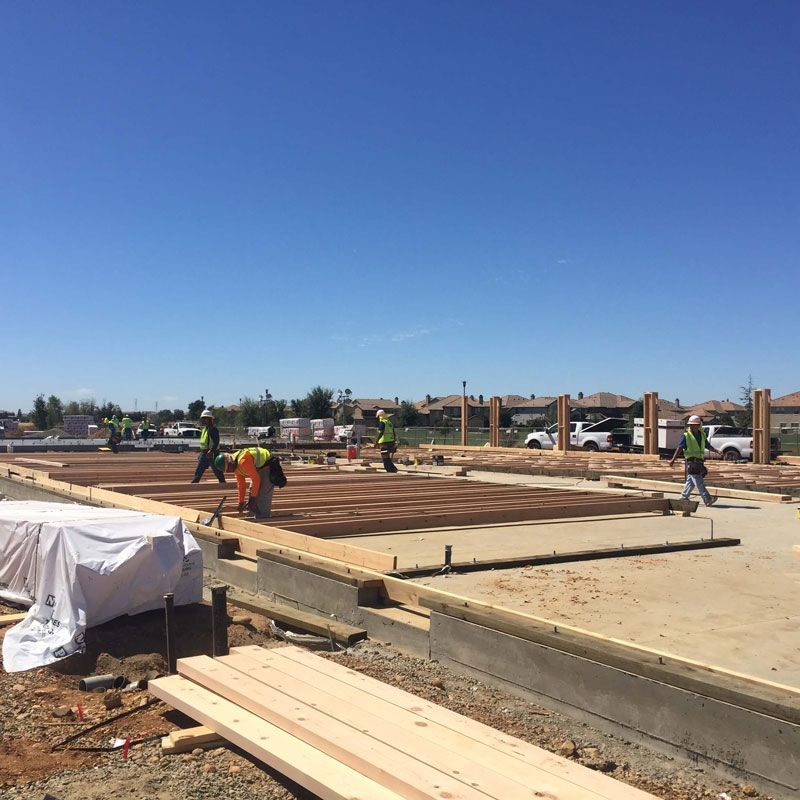 Workers framing a wooden foundation on a construction site under a clear blue sky