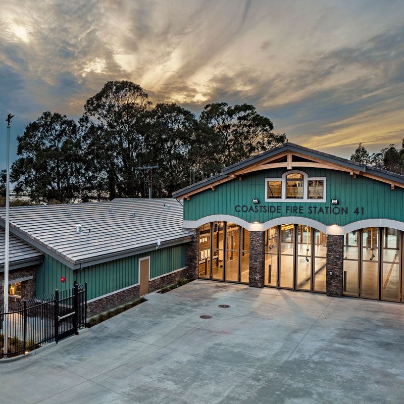 Coastal Fire Station 41 building at dusk, with teal siding, lit garage bays, and a large concrete forecourt